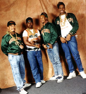 Photo de groupe de 2 Live Crew : quatre membres en blousons verts, chaînes en or et jeans, posant devant un fond beige.