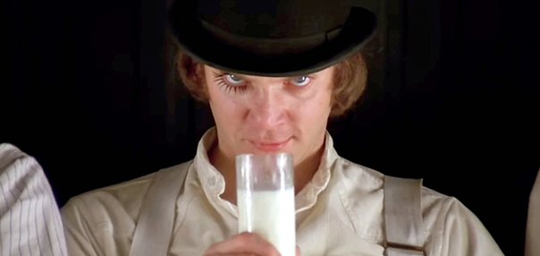 Image du film Orange mécanique : Alex, en chapeau melon et faux cils à un œil, fixe la caméra en buvant un verre de lait.